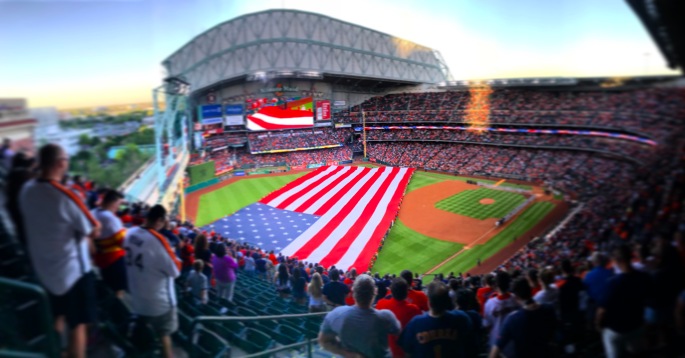 A large American flag expands across the outfield of a baseball stadium before the start of a game.